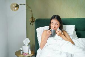 Gesundheit und Personen. asiatisch Mädchen Lügen im Bett, Gefühl krank, Niesen und Trinken heiß Tee, fangen kalt, bleiben beim Zuhause auf verlassen foto