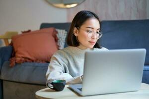 selbst beschäftigt jung Koreanisch Frau Arbeiten auf Fernbedienung, Tippen auf Laptop, studieren beim Zuhause im Leben Zimmer foto