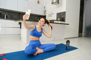 Sport und Lebensstil Konzept. jung Frau tun trainieren beim Zuhause auf Yoga Matte, macht Fitness vlog mit Smartphone, nimmt Selfie auf Handy, Mobiltelefon Telefon foto