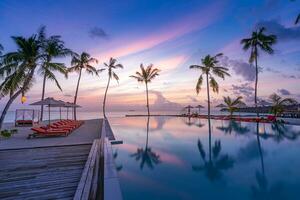 tropischer Sonnenuntergang über Infinity-Außenpool im Sommerbadeort, Strandlandschaft. luxus, ruhiger strandurlaub, reflexion am pool, entspannende chaiselongue, romantischer bunter himmel, stühle, regenschirm foto