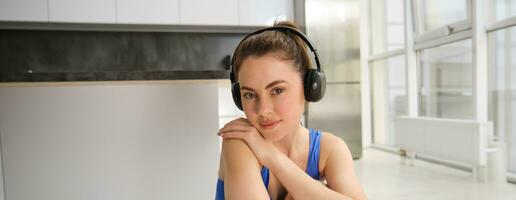 schließen oben Porträt von schön Brünette Mädchen im Sportbekleidung, sitzt im kabellos Kopfhörer und hört zu Musik, während tun trainieren Ausbildung beim Zuhause foto