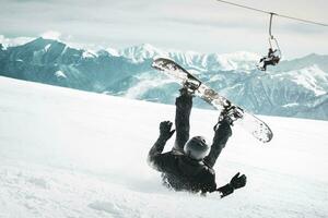 Snowboarder fallen Nieder auf zurück schmerzlich mit Schnee spritzt auf schneebedeckt abseits der Piste Ski Steigung und alt Stuhl Aufzug beim Hintergrund. sonnig Winter Tag. schwarz und Weiß getönt Bild. foto