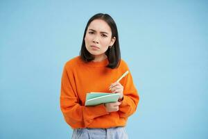 Bildung und Studenten. glücklich asiatisch Frau, halten Notizbücher und Lachen, lächelnd beim Kamera, genießt gehen zu Universität oder Hochschule, Blau Hintergrund foto