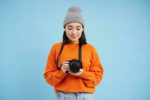 leidenschaftlich asiatisch Mädchen Fotograf, nehmen Bilder auf ihr Digital Kamera, Erfassen Momente draußen, Schießen Fotos, Blau Hintergrund foto