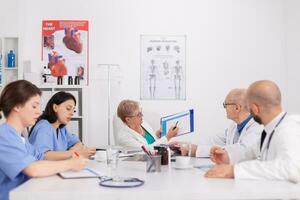 Physiotherapeut Arzt erklären Krankheit Diagnose mit Zwischenablage präsentieren medizinisch Sachverstand während Sitzung beim Schreibtisch im Treffen Zimmer. Kinderarzt Senior Frau erklären Gesundheitswesen Behandlung foto