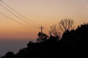 der goldene Himmel in der Abenddämmerung und die Silhouette schwarzer Bäume auf den Bergen foto