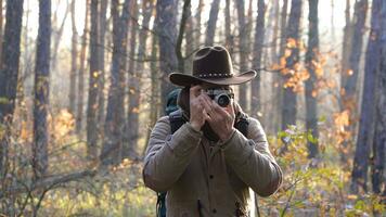 ein Mann im ein Hut mit ein Rucksack nimmt Bilder im das Wald. Nahaufnahme. Reise Konzept foto