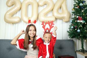 fröhlich Weihnachten 2024 Konzept Mutter und Kind schmücken das Weihnachten Baum mit bunt Weihnachten Bälle. foto