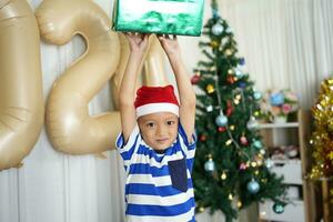 fröhlich Weihnachten 2024 Konzept ein Junge halten ein Geschenk Box ist glücklich zu erhalten ein Geschenk auf Weihnachten Tag. foto