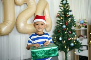 fröhlich Weihnachten 2024 Konzept ein Junge halten ein Geschenk Box ist glücklich zu erhalten ein Geschenk auf Weihnachten Tag. foto