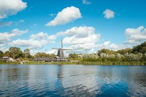 historisch hölzern Windmühle auf das Banken von ein Fluss in der Nähe von Haarlem, im das Westen von das Niederlande. Niederländisch Landschaft auf ein sonnig Tag foto
