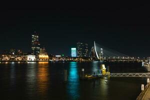 Aussicht von das Kanal und das Gegenteil beleuchtet Bank mit viele von beleuchtet Wolkenkratzer während spät Nacht im Rotterdam, Niederlande foto