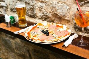 köstlich Pizza mit Prosciutto und Pilze, ein Glas von Bier und ein Glas von Aperol beim draussen Cafe. selektiv Fokus. foto
