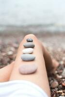 schön glatt Steine Lüge auf ein Frau Bein beim das Meer. das Konzept von Körper Pflege, Meditation und Entspannung. Nahansicht. selektiv Fokus. foto