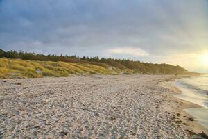 Sonnenuntergang auf das Westen Strand auf das baltisch Meer. Wellen, Strand, wolkig Himmel und Sonnenschein foto