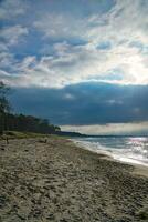 Sonnenuntergang auf das Westen Strand auf das baltisch Meer. Wellen, Strand, wolkig Himmel und Sonnenschein foto