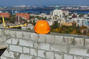 Orange schwer Hut ist auf ein Backstein Mauer. Dach von modern Gebäude unter Konstruktion. malerisch Panorama- Stadtbild, Blau Himmel, sonnig Tag foto