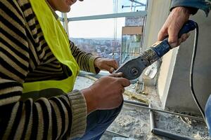 zwei Unbekannt Arbeitskräfte im Arbeitskleidung mit Löten Eisen zum Plastik Rohre oder Rohr Schneiden Schere im ein eben von Hochhaus Gebäude unter Konstruktion foto