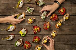 Hände nehmen Bruschettas mit verschiedene Belag auf hölzern Oberfläche foto