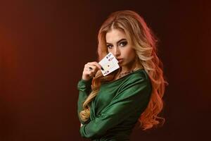 blond weiblich im Grün stilvoll Kleid und Schmuck. zeigen zwei spielen Karten, posieren seitwärts auf braun Studio Hintergrund. Poker, Kasino. Nahansicht foto