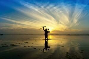 minimal Silhouette von glücklich Tourist mit Stangen im Hand über Kopf auf das Strand mit Sonnenaufgang Himmel. foto