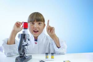 ein wenig Mädchen im ein Labor Mantel erhöht ein Finger hoch. das Konzept von Lernen und wissenschaftlich Erfolge. foto