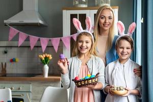 glückliche Mutter und ihre lächelnden, lieben Kinder, die bunte Eier halten und wirklich frohe Ostern foto