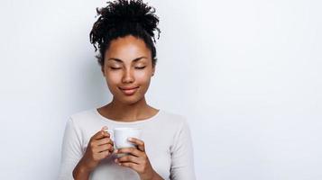Schönes afroamerikanisches Mädchen, das einen Biobecher hält und die Augen schließt und ein Getränk auf weißem Hintergrund genießt