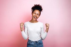 überglückliches afroamerikanisches tausendjähriges Mädchen, das auf rosa Studiohintergrund isoliert ist, Triumph gute Nachrichten erhalten. Gewinnerkonzept foto