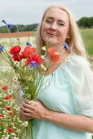 schön mittleren Alters blond Frau steht unter ein blühen Feld von Mohnblumen foto