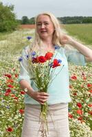 schön mittleren Alters blond Frau steht unter ein blühen Feld von Mohnblumen foto