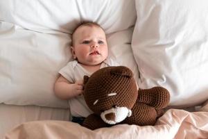 süßes, schönes kleines Mädchen, das mit einem Teddybären auf dem Bett liegt foto