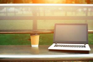 Attrappe, Lehrmodell, Simulation Bild von Laptop mit leer schwarz Bildschirm und Kaffee Tasse auf Metall Bank im Natur draussen Park foto