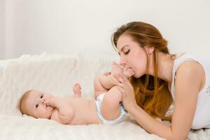 Mutter und Kind auf ein Weiß Bett. Mama und Baby Mädchen im Windel spielen im sonnig Schlafzimmer. foto