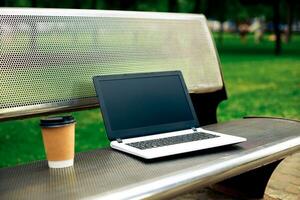Attrappe, Lehrmodell, Simulation Bild von Laptop mit leer schwarz Bildschirm und Kaffee Tasse auf Metall Bank im Natur draussen Park foto