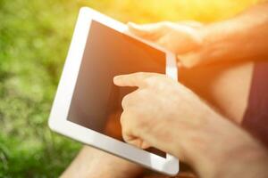 jung Hipster Junge Sitzung im das Park und mit modern Digital Tablette foto