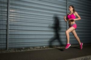 Laufen Frau. Joggen gegen das Hintergrund von ein grau Mauer foto