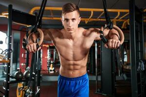 Porträt von jung Mann mit Gymnastik- Ringe während ausüben im Fitnessstudio foto