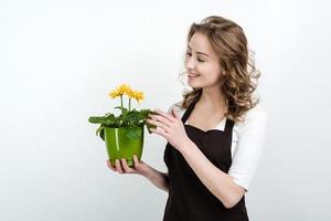 lächelndes Mädchen in der Schürze, die blühenden Blumentopf lokalisiert auf weißem Hintergrund hält. foto