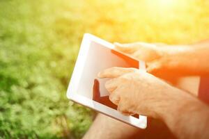 Nahansicht von beiläufig gekleidet jung Mann mit modern Digital Tablette während Sitzung beim das Park, Sonne Licht foto