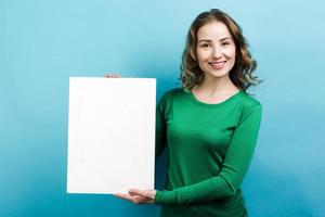 junge schöne Frau mit weißem Gegenstand auf der Hand auf blauem Hintergrund foto