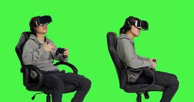 Spieler haben Spaß mit vr Kopfbedeckung und Regler, spielen online Spielen Wettbewerb mit andere Personen. asiatisch Person genießen Freizeit Aktivität während er sitzt auf Stuhl gegen grüner Bildschirm Hintergrund. foto