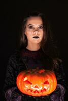 attraktiv Frau mit ein ernst Gesicht gekleidet oben mögen ein Hexe halten ein Kürbis Über schwarz Hintergrund. foto