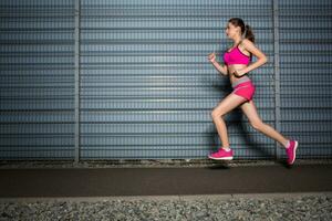 Laufen Frau. Joggen gegen das Hintergrund von ein grau Mauer foto