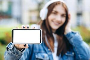 Nahaufnahme eines Mädchens in Kopfhörern auf einem unscharfen Hintergrund zeigt einen weißen Telefonbildschirm, Kopierraum foto