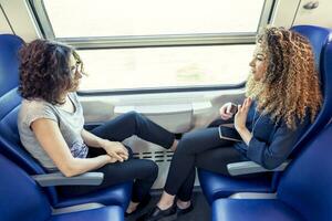 zwei lächelnd schön Mädchen sich unterhalten zu jeder andere Sitzung im ein Wagen Zug foto