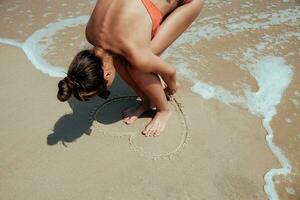 Sommer- Mädchen Meer. Teenager zeichnen Herz auf Sand. foto