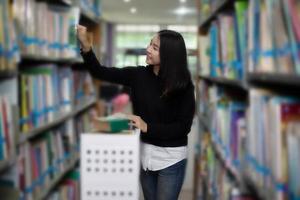 Asiatische Studentinnen, die in der Bibliothek ein Buch zur Auswahl halten