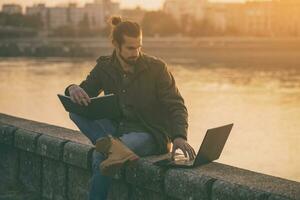 gut aussehend Geschäftsmann mit persönlich Veranstalter und Laptop während Sitzung durch das Fluss.getönt Bild foto