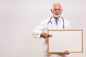 Porträt von Senior Arzt halten Weiß Tafel auf grau Hintergrund. foto